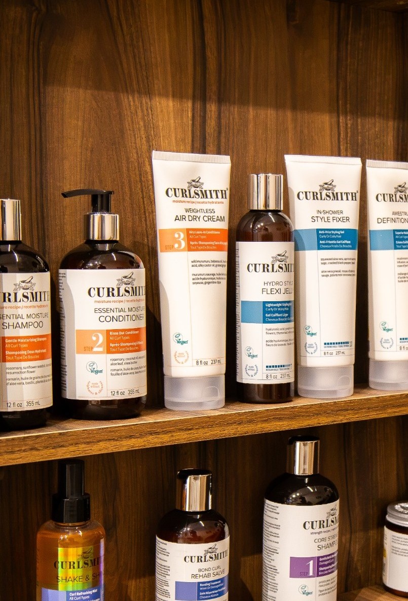 Curlsmith curl-care products on the upper shelves at Hair by Desailee